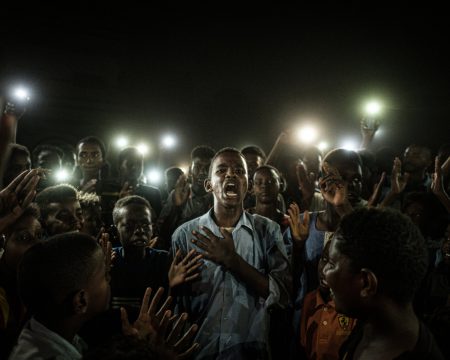 Sudański nastolatek recytuje wiersz na proteście w Chartumie oświetlany przez światło smartfonów