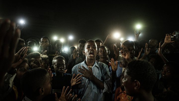 Sudański nastolatek recytuje wiersz na proteście w Chartumie oświetlany przez światło smartfonów